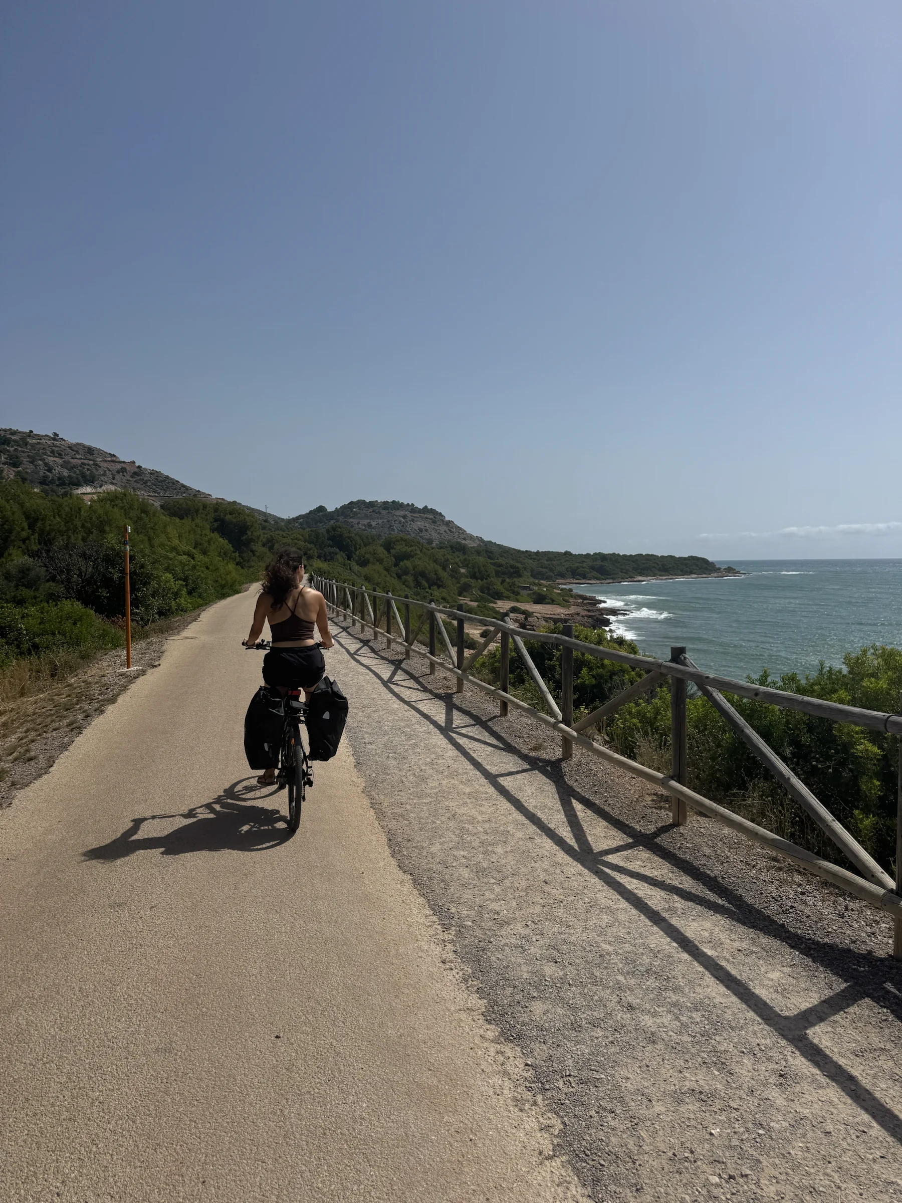 Ein Radfahrer auf einem bepackten Rad auf einem stillen Küstenweg am Mittelmeer.
