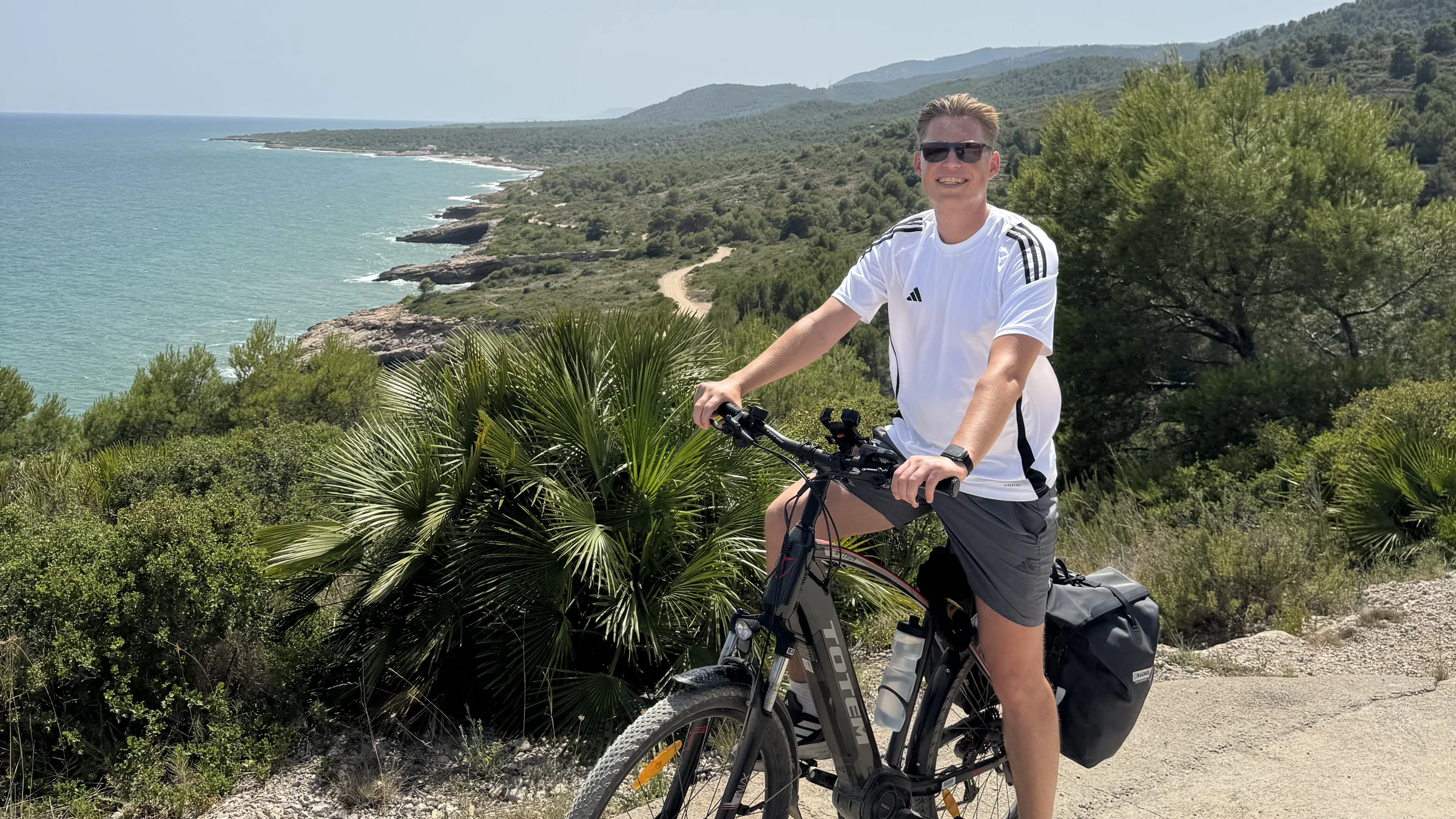 Radfahrer mit bepacktem Trekking-E-Bike mit Blick auf die Mittelmeerküste bei Valencia.
