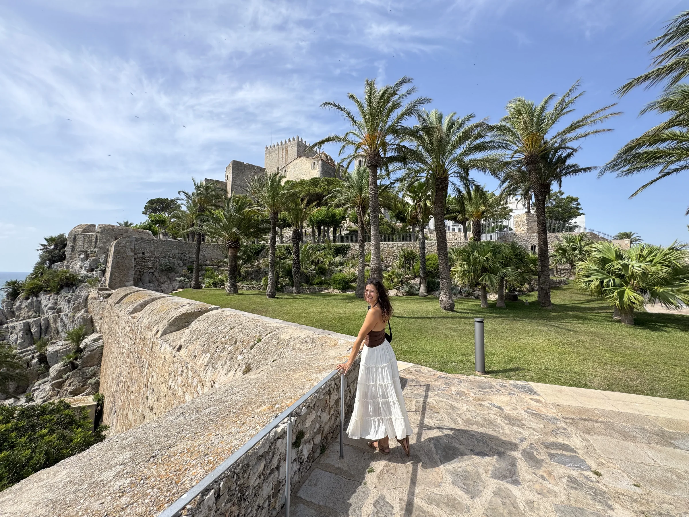 Reisender auf einem palmengesäumten Weg neben der Burg von Peñíscola und dem Meer.