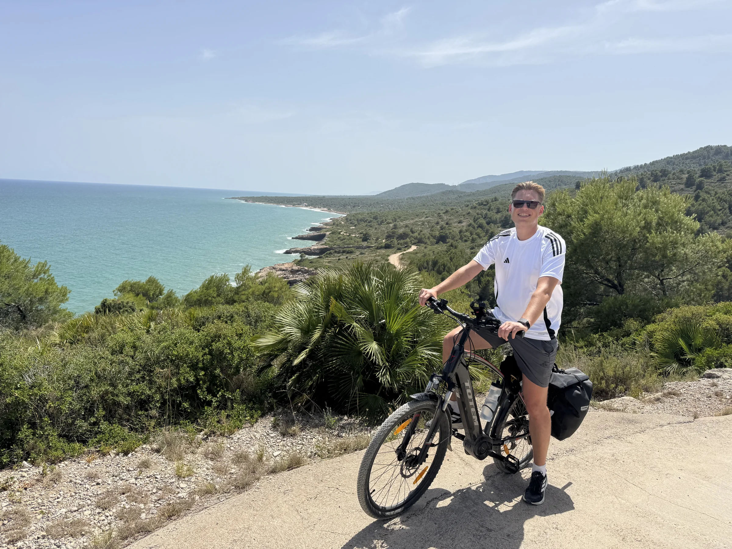 Fahrer mit bepacktem E-Bike über der grünen Costa Azahar Küste bei Valencia.